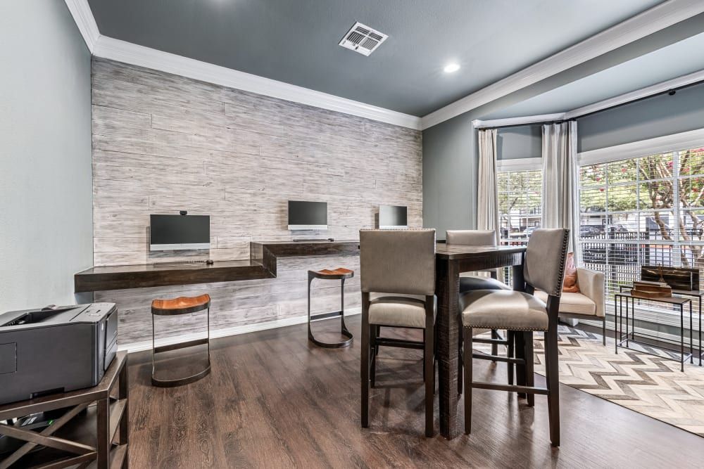 a living room with a table and chairs and computers on the wall at Marquis at Deerfield in San Antonio, TX.