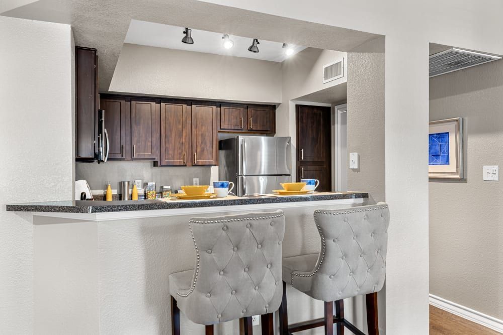 a kitchen with two bar stools and a refrigerator at Marquis at Deerfield in San Antonio, TX.