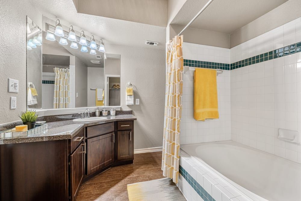a bathroom with a tub, sink, mirror, and shower curtain at Marquis at Deerfield in San Antonio, TX.