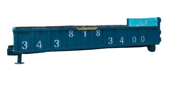 A dumpster is sitting in a dirt field with a bulldozer in the background.