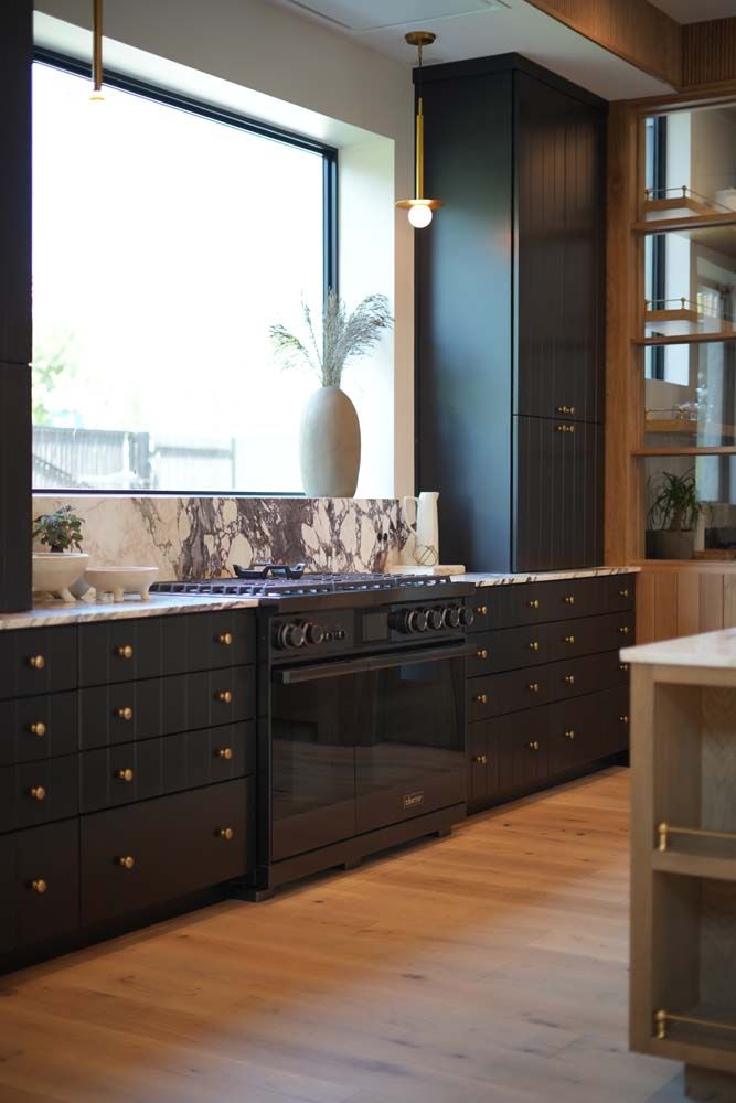 A kitchen with black cabinets , a black stove and a large window.