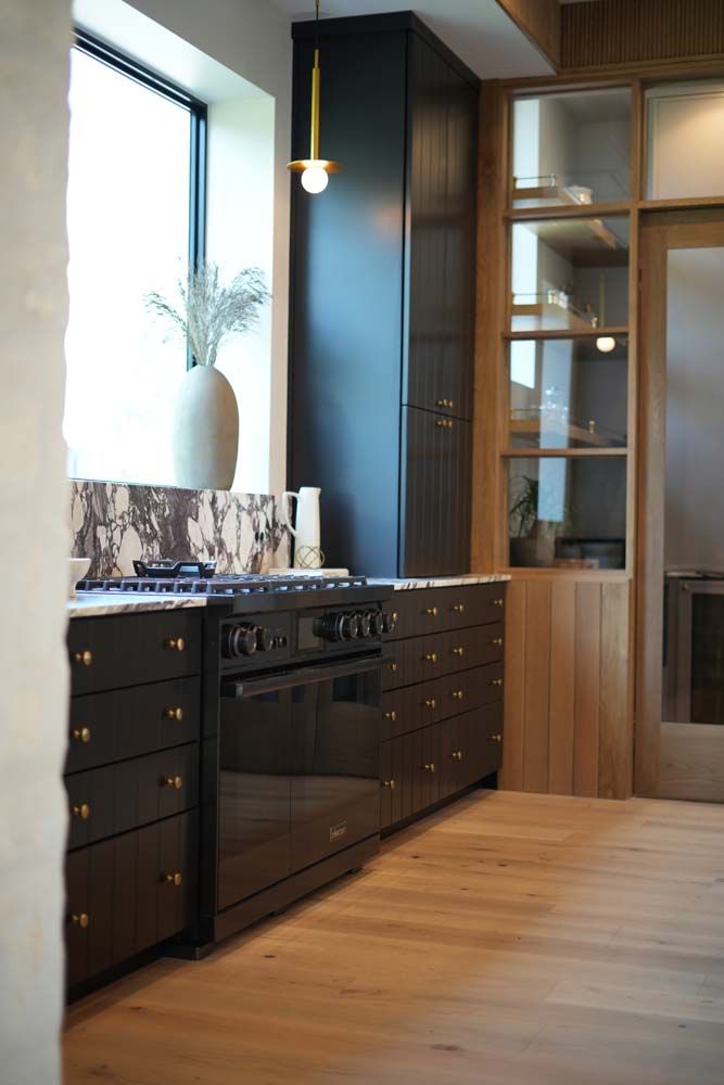 A kitchen with black cabinets , a stove , and a window.
