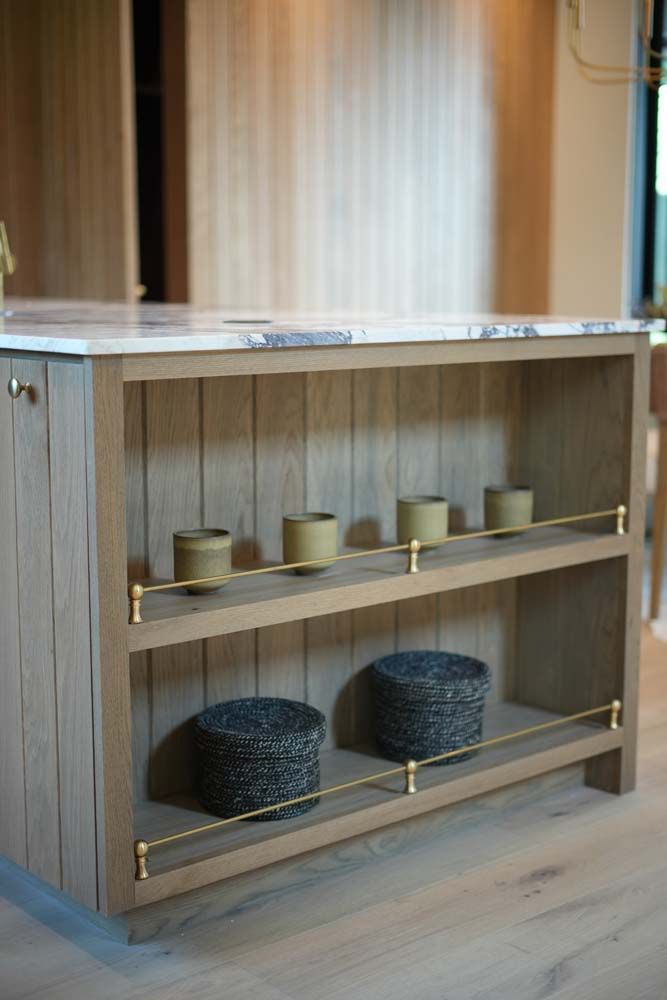 A wooden shelf with candles and baskets on it in a kitchen.