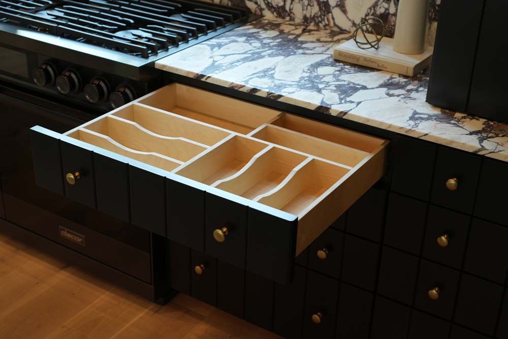 A kitchen with black cabinets and a wooden drawer open