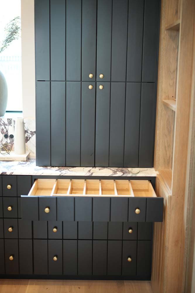 A kitchen with black cabinets and wooden drawers.