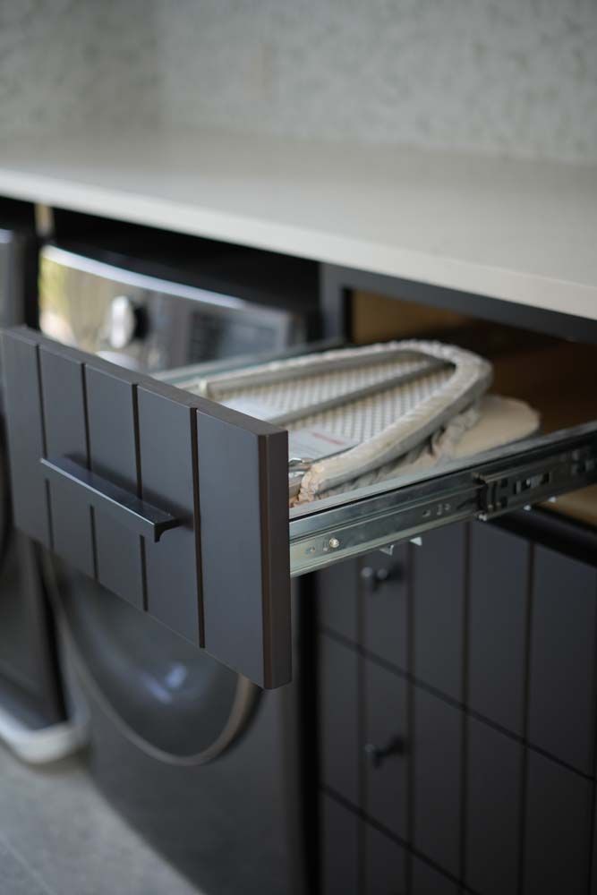 An ironing board is sitting in a drawer next to a washing machine.