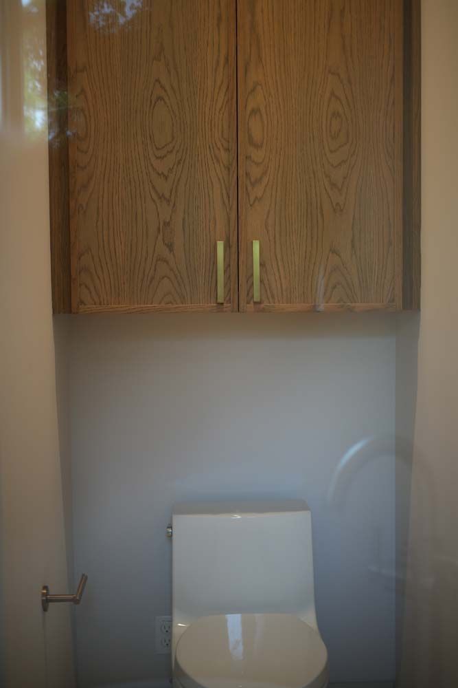 A toilet in a bathroom with wooden cabinets above it.