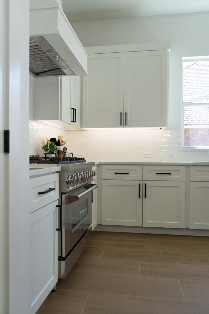 A kitchen with white cabinets , a stove , and a window.