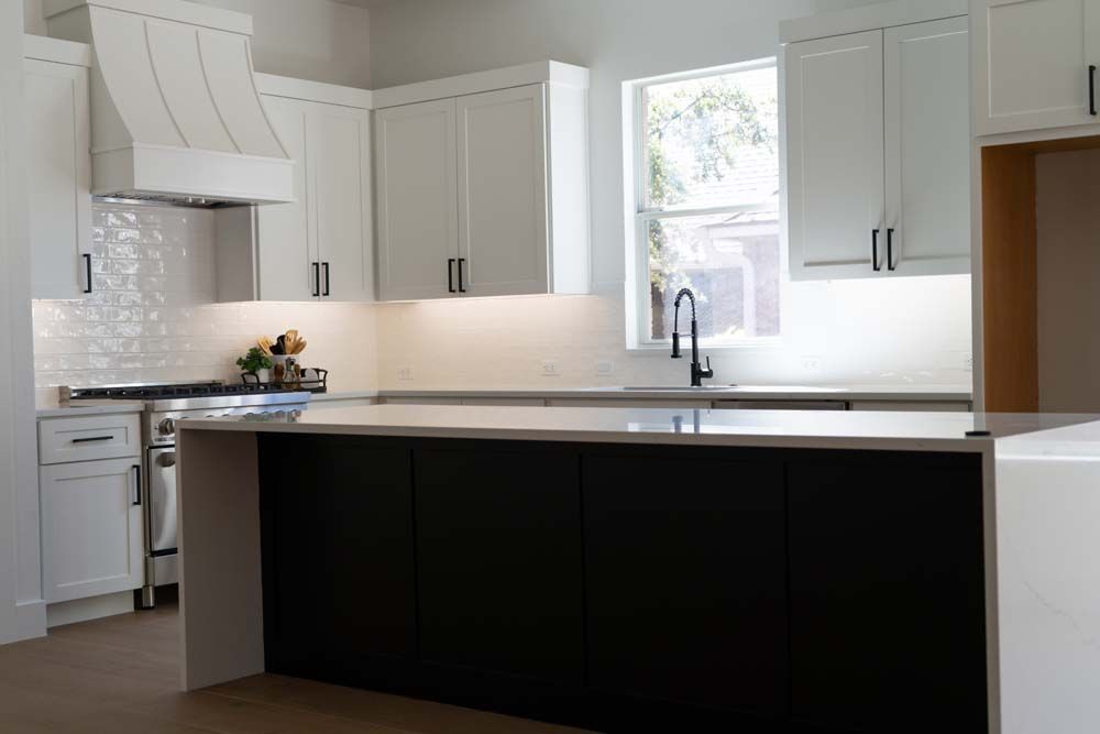A kitchen with white cabinets and black counter tops and a large island.