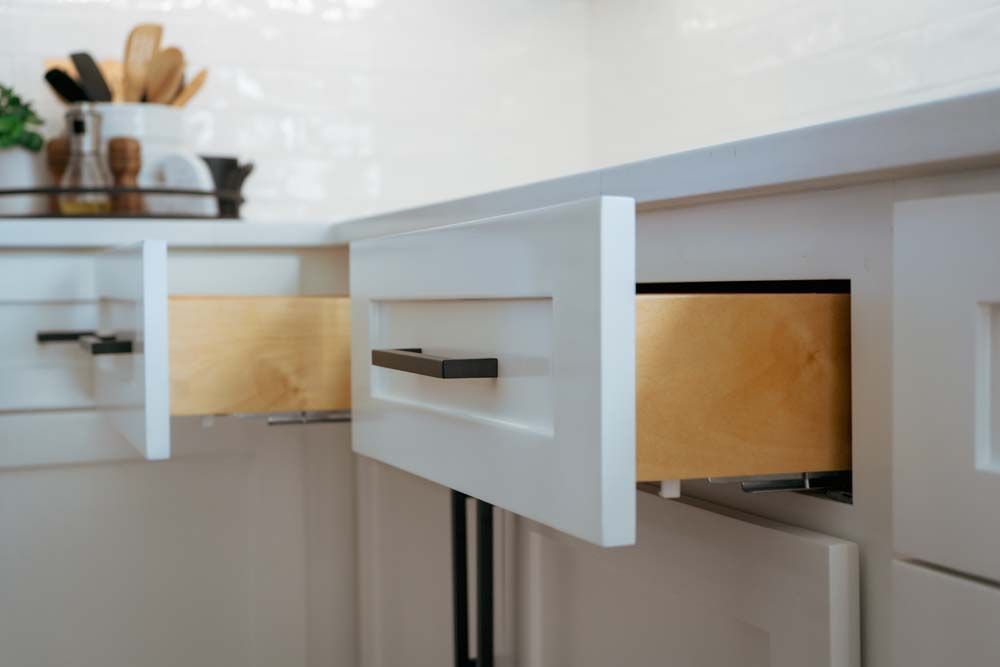 A kitchen with white cabinets and a drawer open.