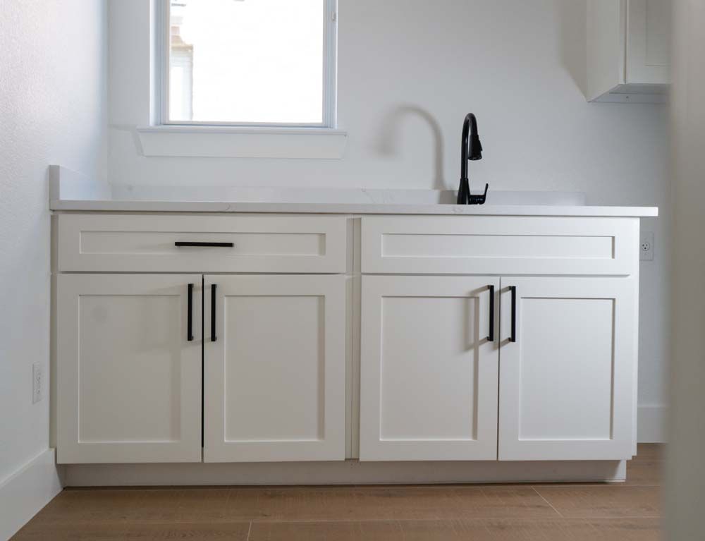 A kitchen with white cabinets and a black faucet
