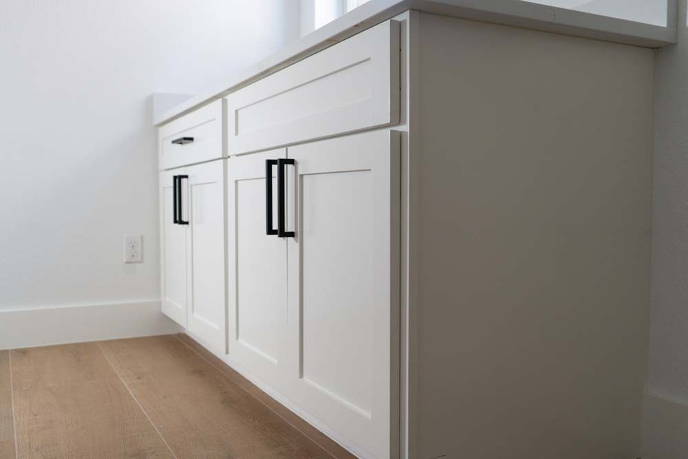 A bathroom vanity with white cabinets and black handles.