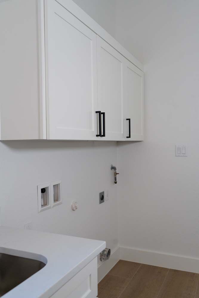 A laundry room with white cabinets and a sink.