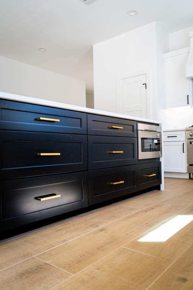 A kitchen with black cabinets and gold handles and a wooden floor.