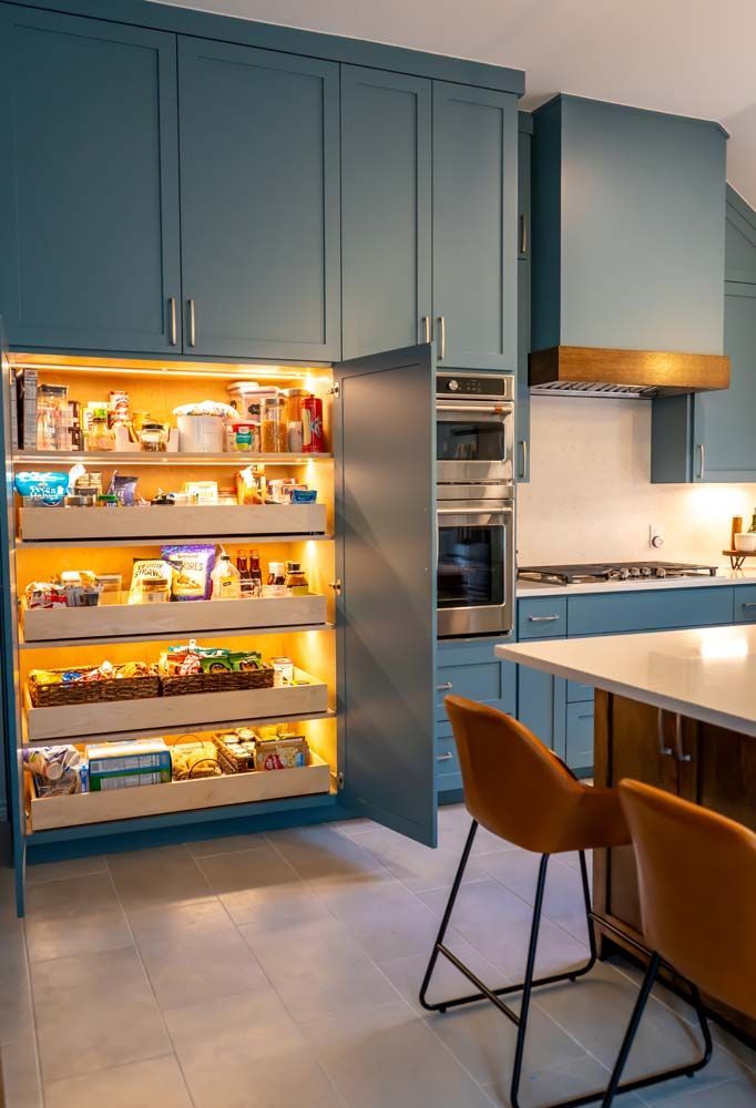 A kitchen with blue cabinets and a pantry with lots of food in it.
