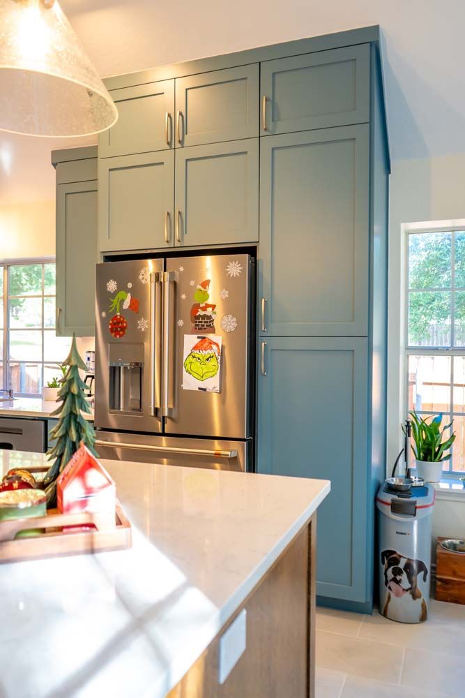 A kitchen with blue cabinets and a stainless steel refrigerator.