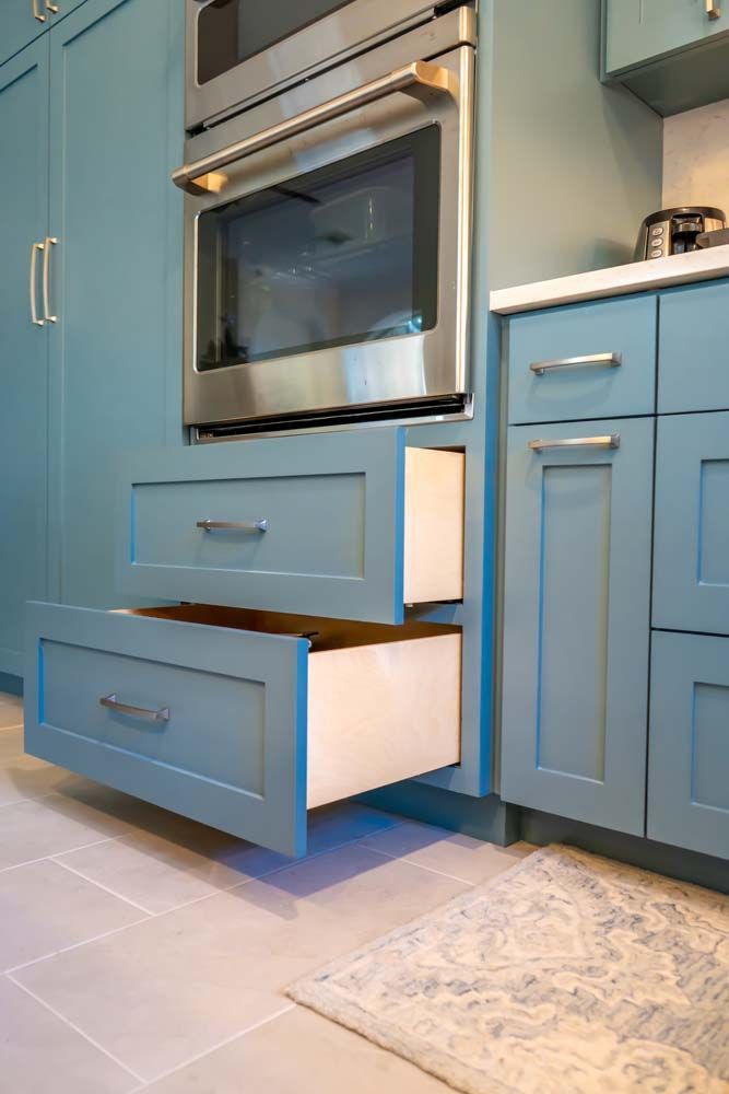 A kitchen with blue cabinets and stainless steel appliances and two drawers open.