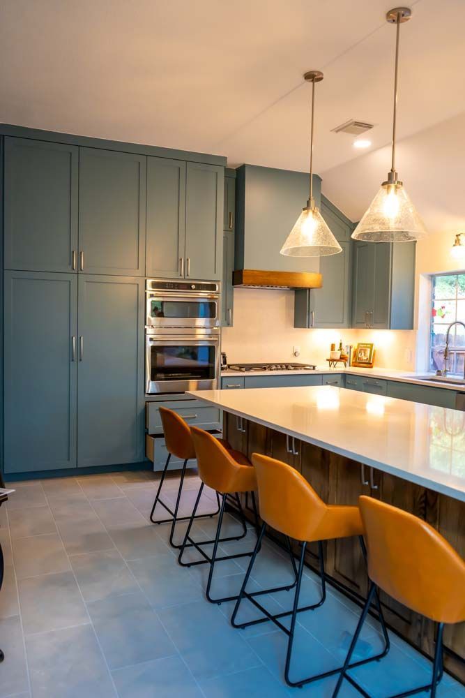 A kitchen with blue cabinets , a large island , and yellow chairs.