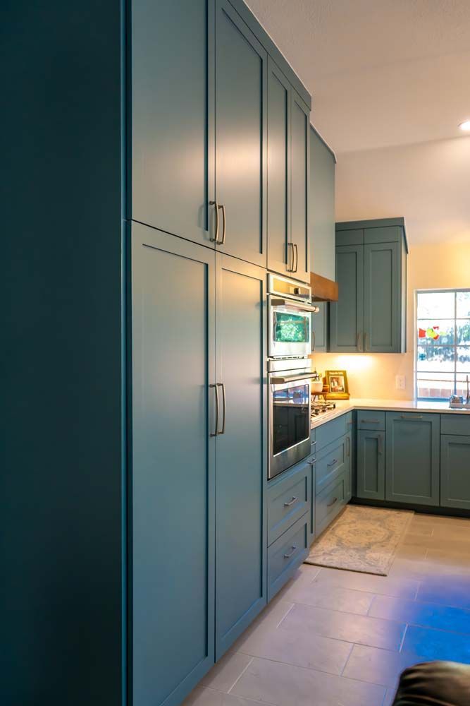 A kitchen with blue cabinets , a microwave oven , and a window.