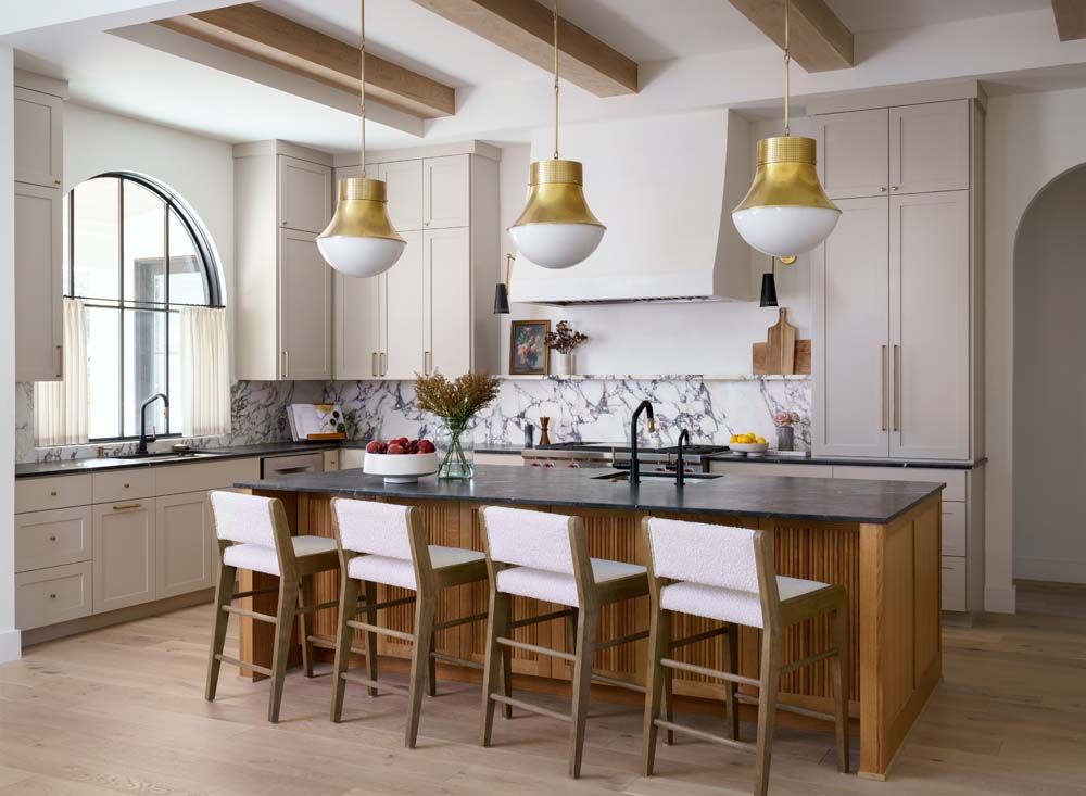 A kitchen with a large island , stools and pendant lights.