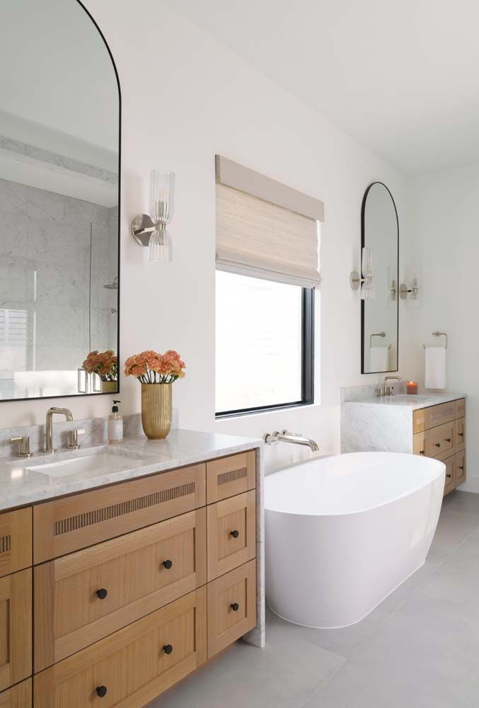 A bathroom with a tub , sink , mirror and window.
