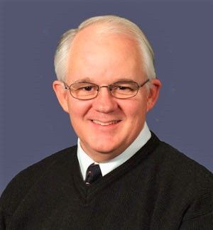 A man wearing glasses and a black sweater smiles for the camera