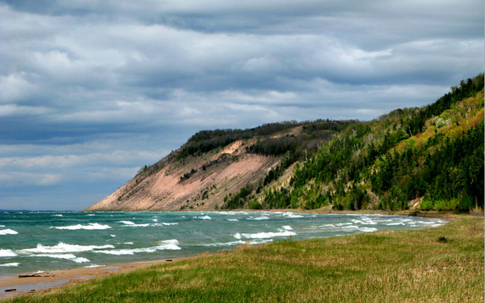 A large body of water surrounded by mountains and trees on a cloudy day.