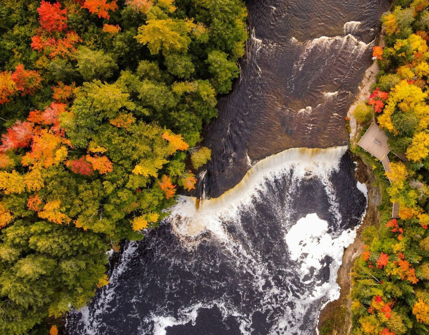 An aerial view of a waterfall surrounded by trees in autumn.