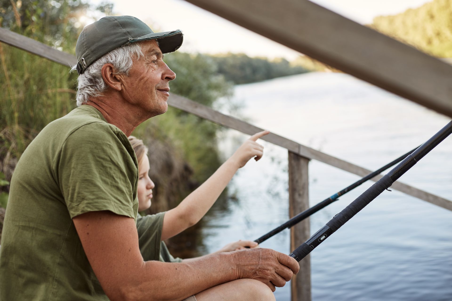 An elderly man and a young boy are sitting on a pier fishing.