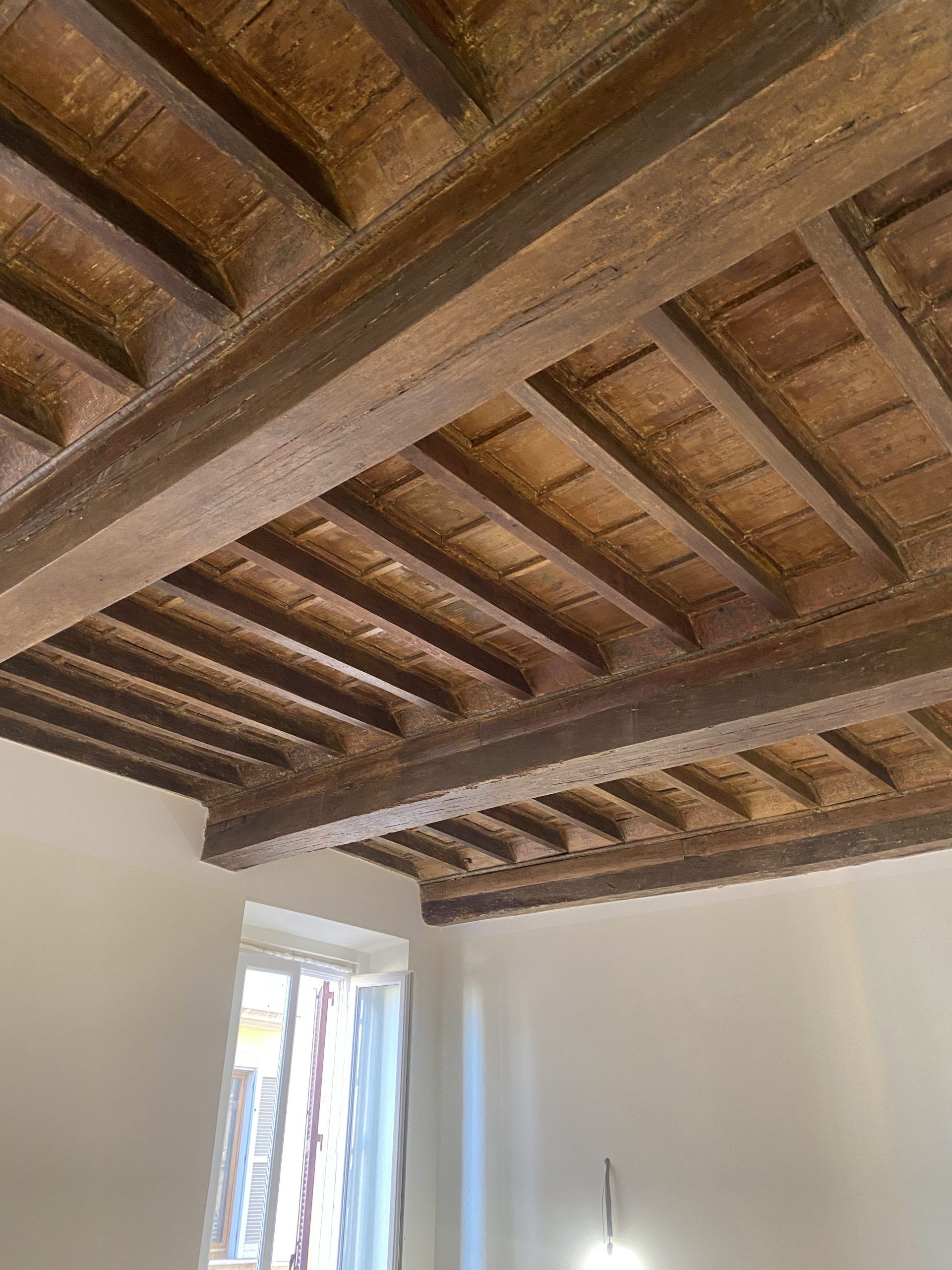 Soffitto con travi in ​​legno e piastrelle in terracotta sopra una stanza bianca con finestra
