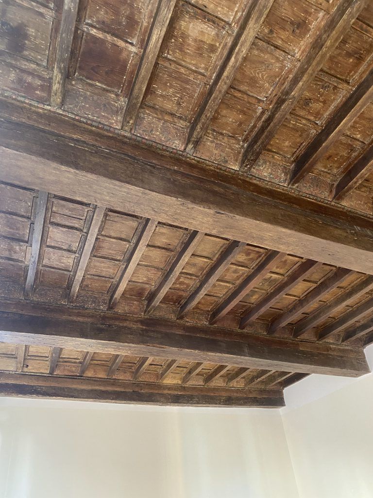 Soffitto con travi in ​​legno scuro a vista sopra pareti bianche e semplici.