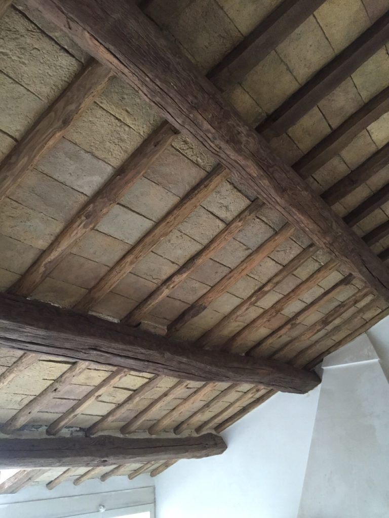 Soffitto con travi in ​​legno antiche e travetti a vista sopra pareti bianche