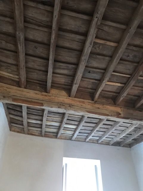 Travi in ​​legno a vista sul soffitto, sopra una parete bianca e un'apertura finestrata all'interno di una stanza.
