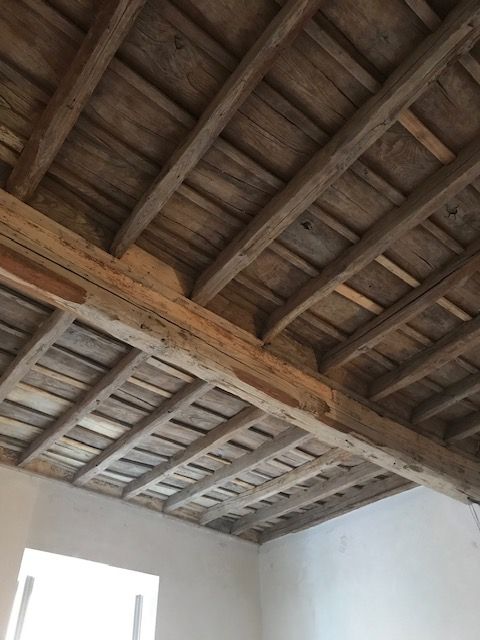 Soffitto con travi in ​​legno a vista sopra pareti interne bianche e una luminosa apertura finestrata.