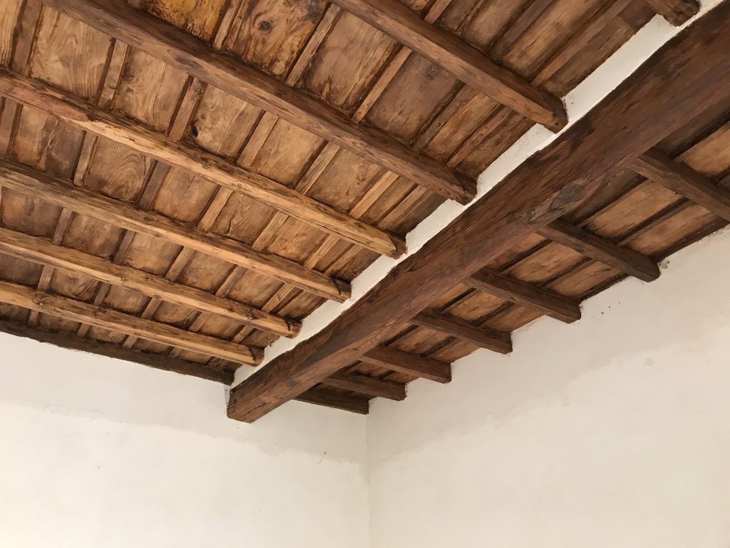 Travi in ​​legno a vista e piastrelle in terracotta sopra pareti bianche in una stanza rustica