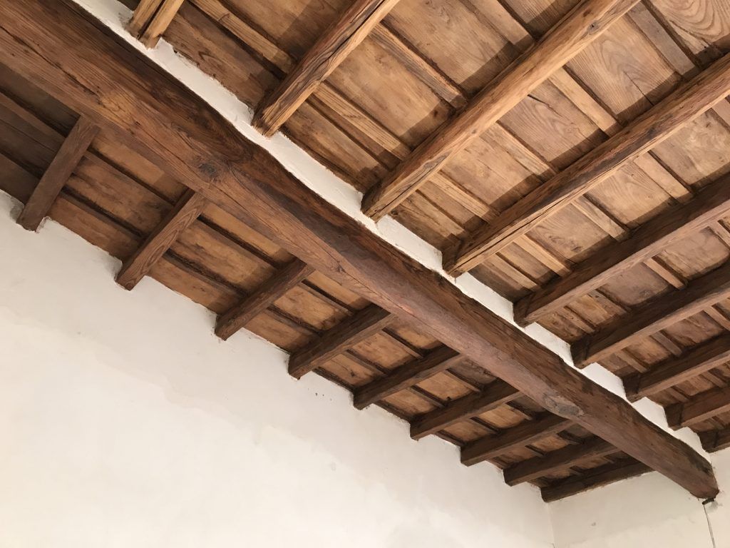 Soffitto con travi in ​​legno e tegole in terracotta sopra una parete bianca.