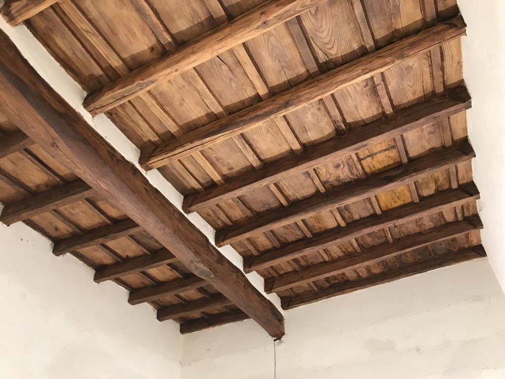 Travi in ​​legno a vista e tegole in terracotta sopra pareti bianche in un interno rustico