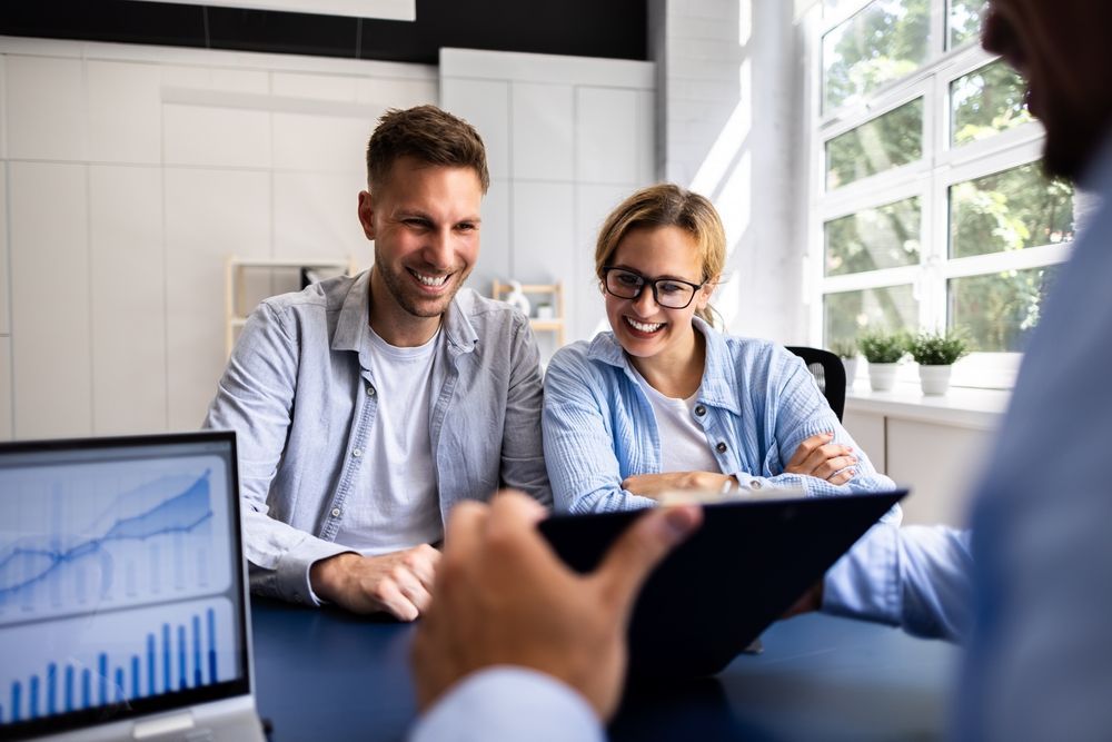 Couple smiles while reviewing documents with a professional at a desk.