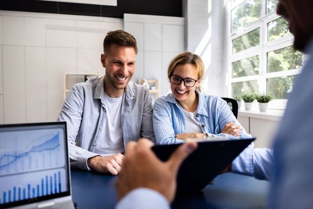 Couple smiles while reviewing documents with a professional at a desk.