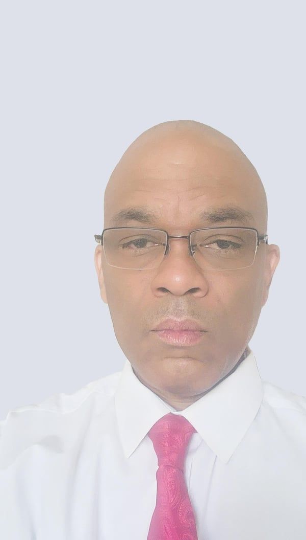 Man with glasses, bald head, and pink tie against a white background.
