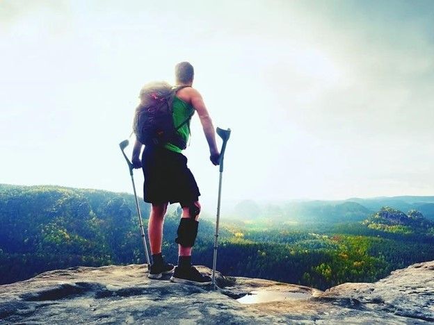 a man with crutches is standing on top of a mountain .