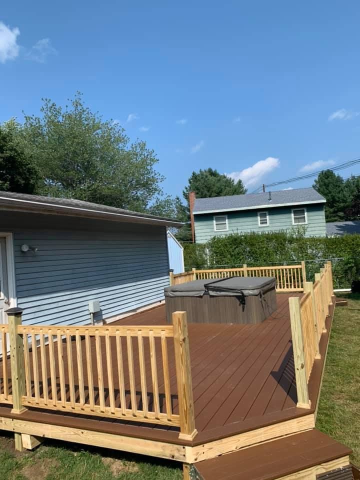 A wooden deck with a built-in hot tub, attached to a house with blue siding under a bright blue sky.
