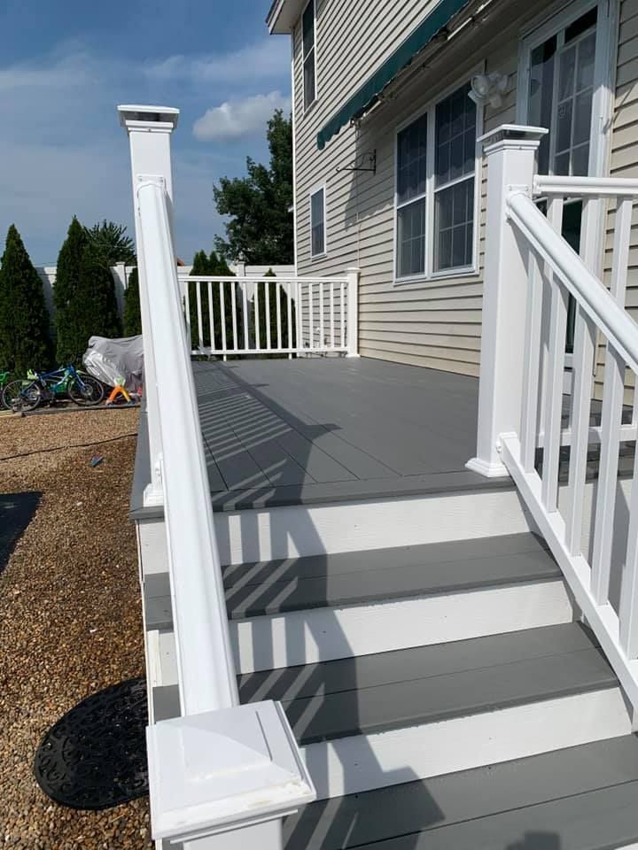 Gray composite deck with white railings and stairs leading to a house exterior under a blue sky.