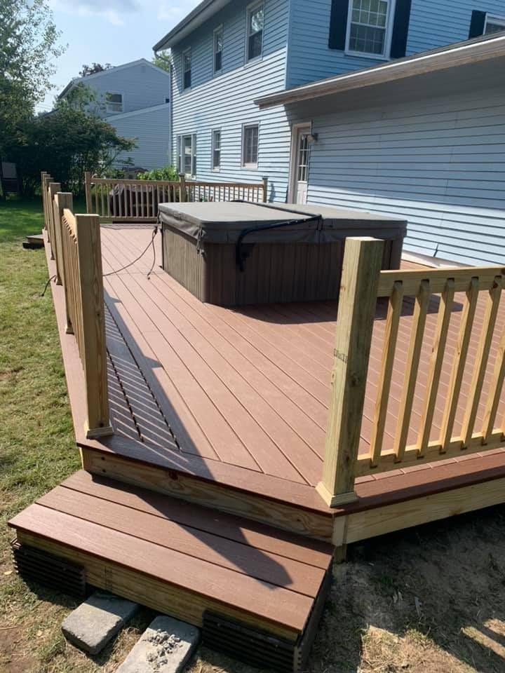 A wooden deck featuring a hot tub in a grey cover, surrounded by railings, with stairs leading down to a grassy yard.