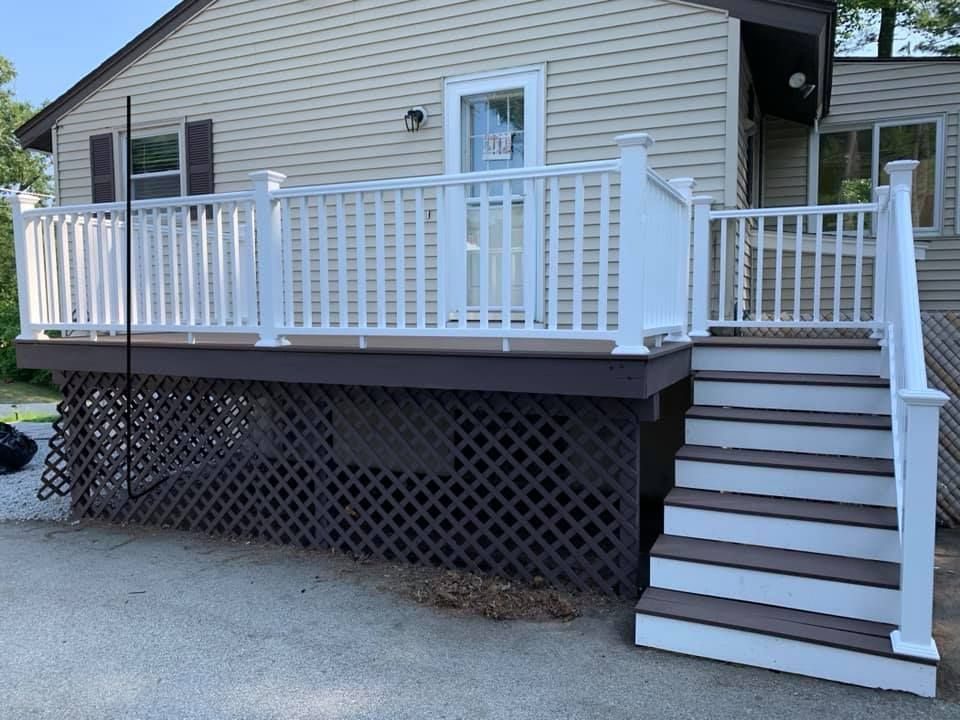 A raised deck with white railings and stairs, a brown wooden base, and brown-and-white steps, attached to a beige house.