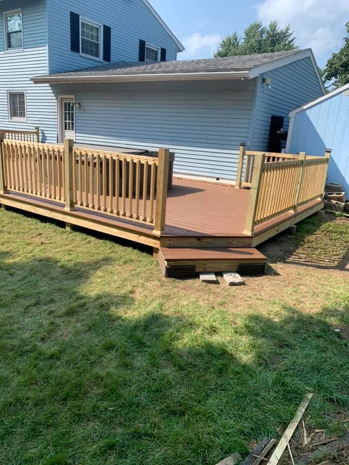 A newly constructed wooden deck with brown composite boards and light wood railings attached to a blue two-story house.