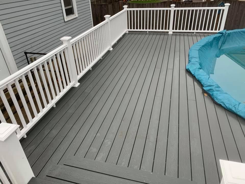 A grey composite deck with white railings wraps around the edge of a swimming pool covered with a blue tarp.