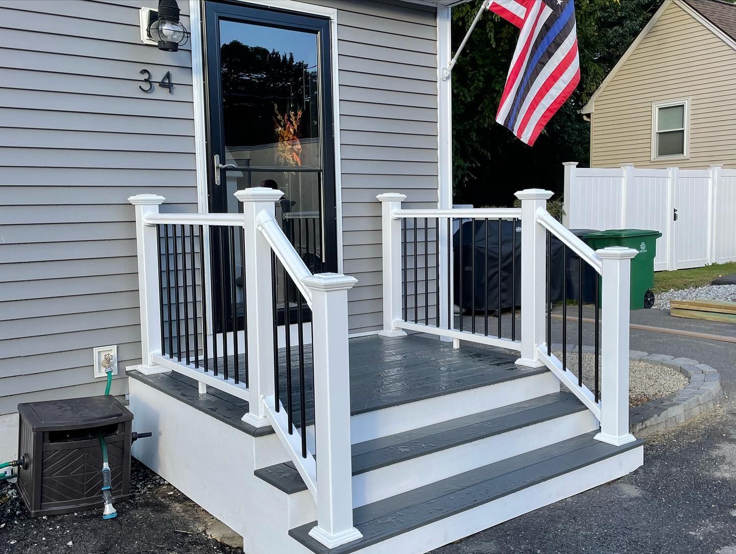 A gray house exterior with a small wooden porch featuring white railings, black balusters, and gray steps.