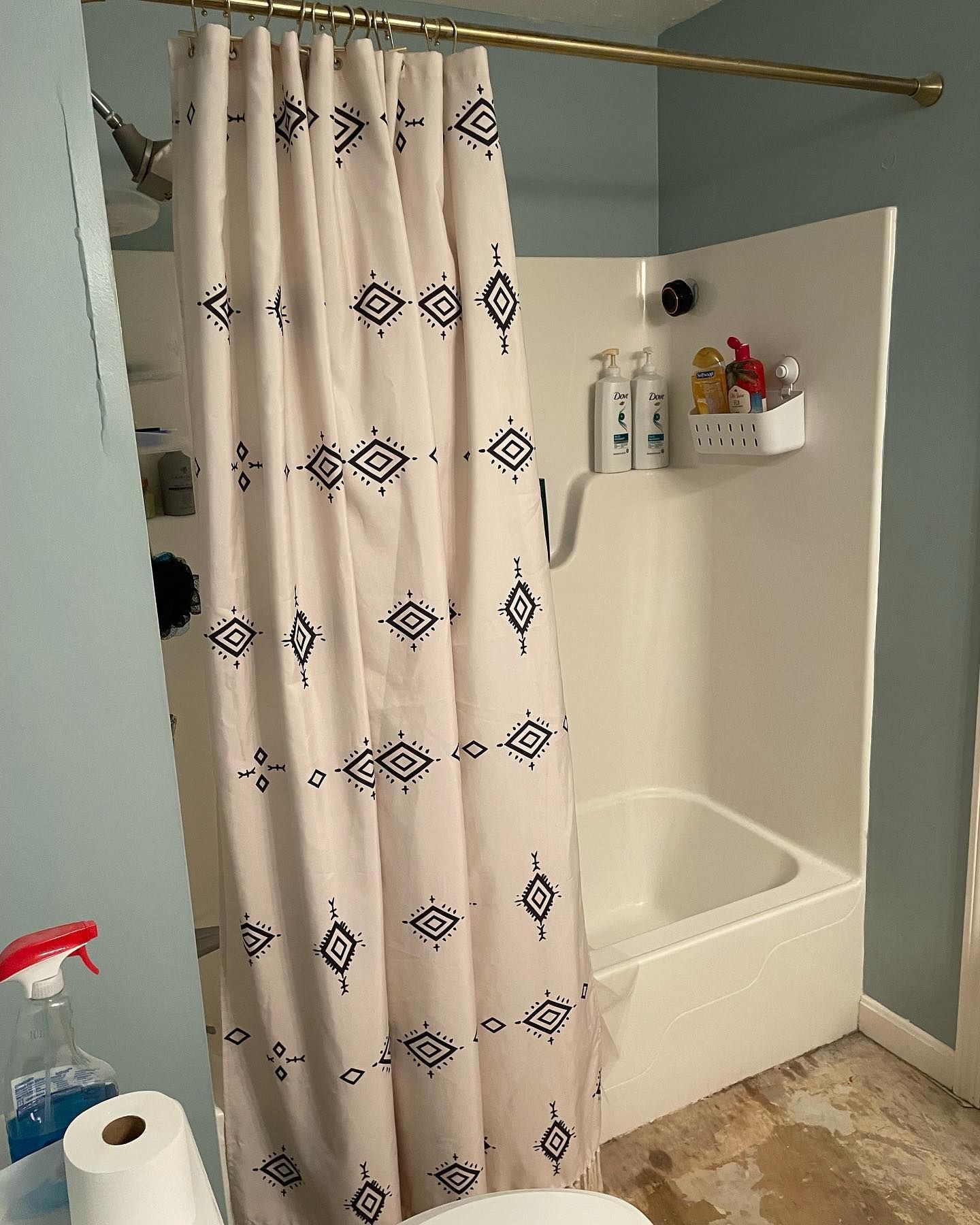 A shower with a beige curtain featuring black geometric patterns, set against light blue walls.