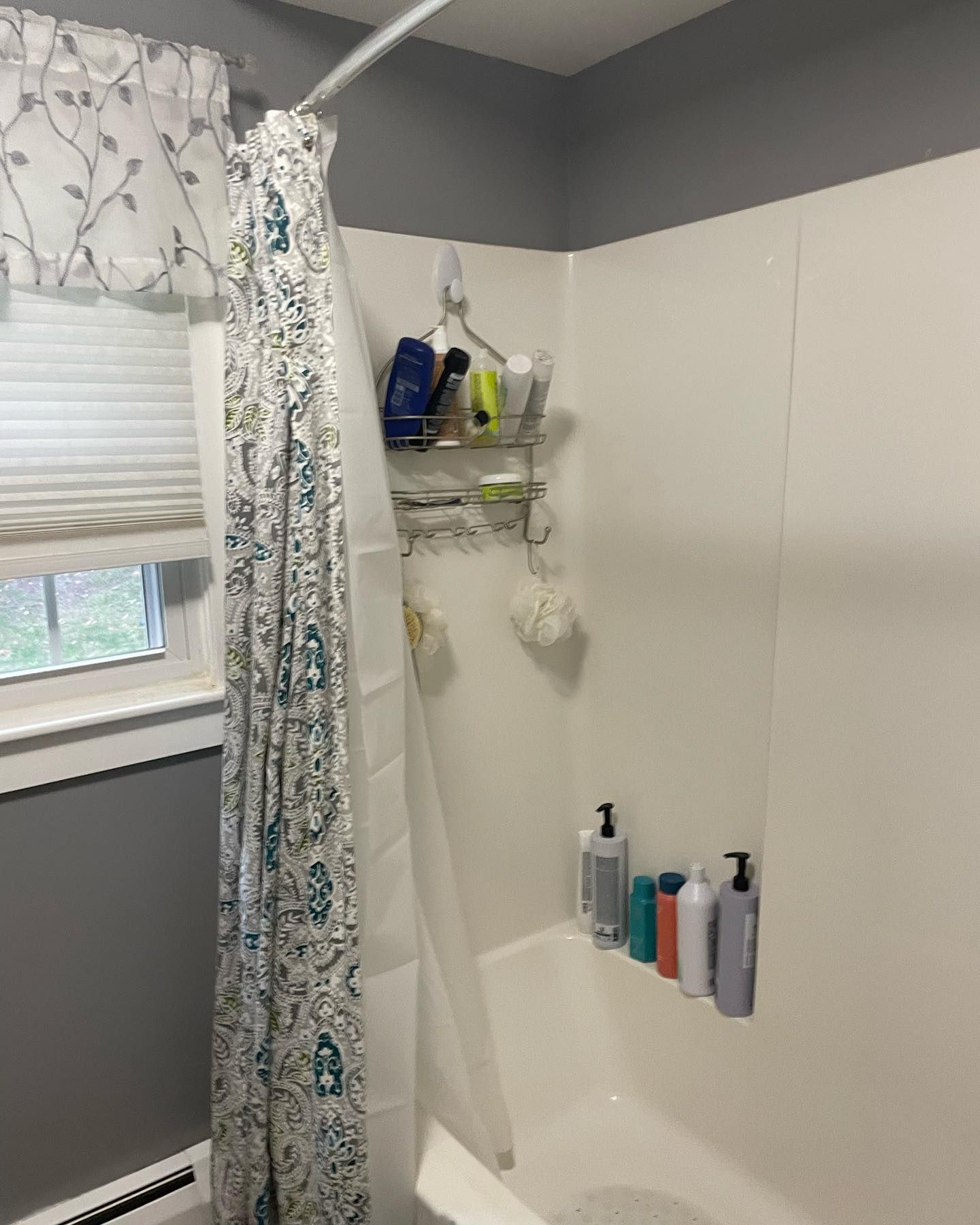A shower stall with a patterned curtain, a metal hanging caddy, and various soap bottles on a built-in ledge.